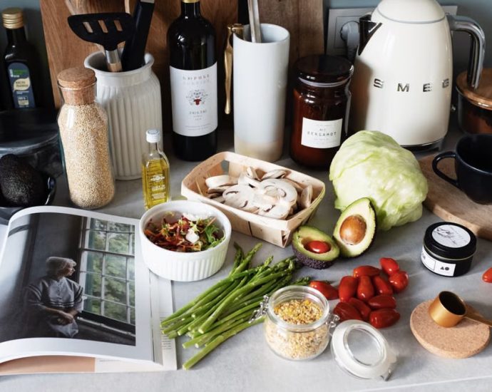 Various colorful healthy food and vegetables locating on countertop next to many different utensils and white kettle during cooking in stylish kitchen