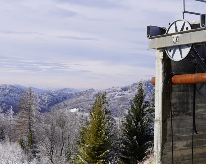 Snow-covered mountains and trees with a concrete industrial structure in view.