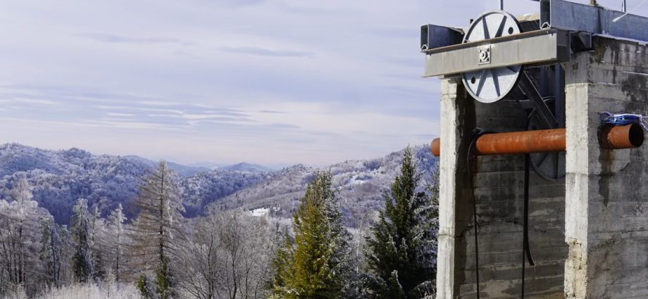 Snow-covered mountains and trees with a concrete industrial structure in view.